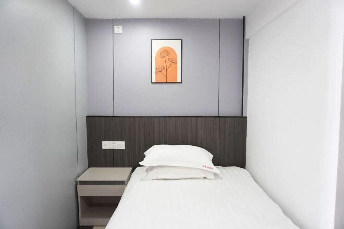Une chambre d’hôtel avec un lit, une table de chevet, un tableau encadré au mur et un interrupteur.