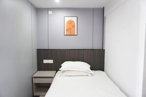 Une chambre d’hôtel avec un lit, une table de chevet, un tableau encadré au mur et un interrupteur.
