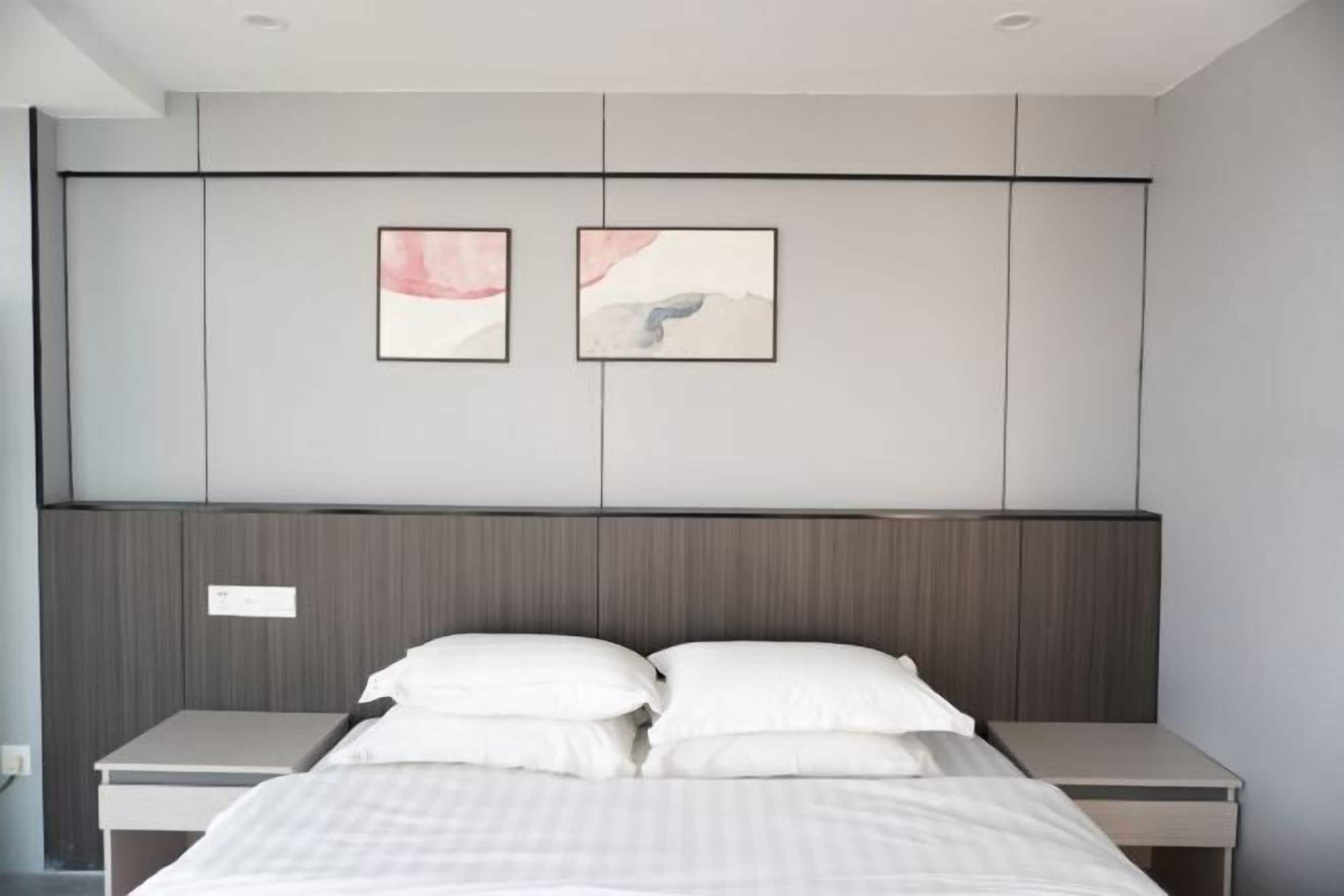 Un dormitorio moderno con una cama, dos mesitas de noche, un cabecero de madera y dos obras de arte enmarcadas en la pared.