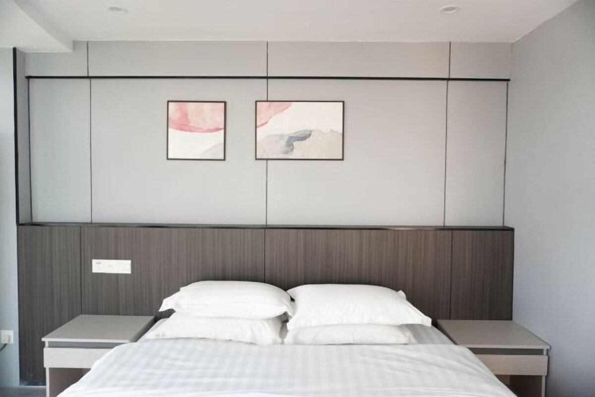 Une chambre à coucher moderne avec un lit, deux tables de chevet, une tête de lit en bois et deux œuvres d’art encadrées accrochées au mur.