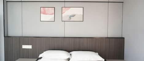 A modern bedroom with a bed, two nightstands, a wooden headboard, and two framed artworks on the wall.