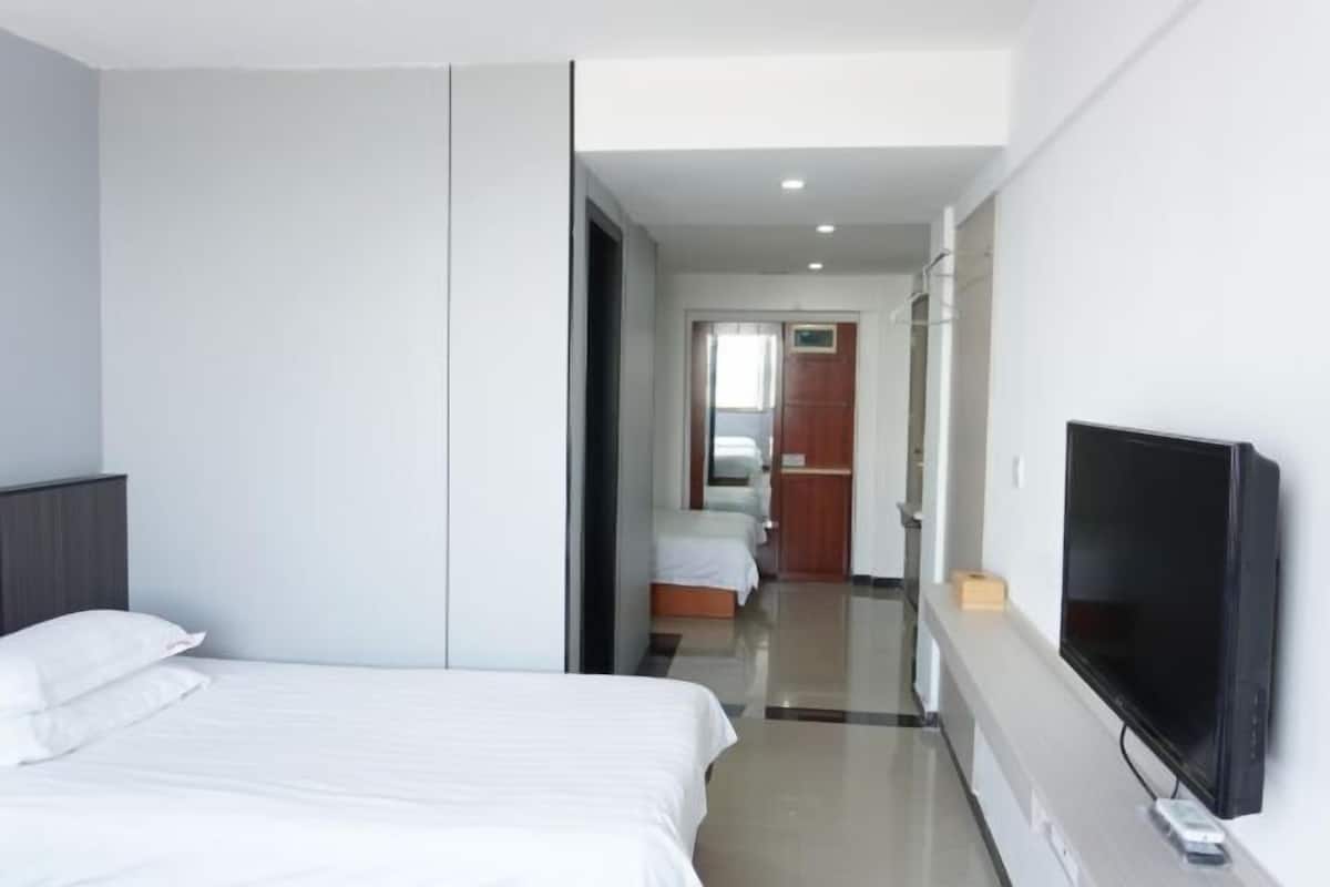 Ein Hotelzimmer mit Bett, Fernseher, Kleiderschrank und einem zur nächsten Kammer führenden Gang.