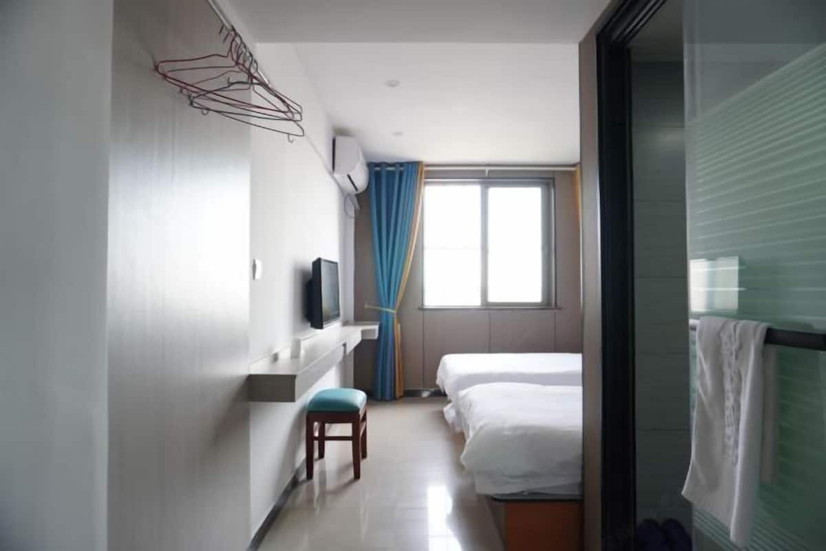 Ein Hotelzimmer mit einem Bett, einem Schreibtisch mit Stuhl, einem Fernseher und einem Fenster mit Vorhängen.