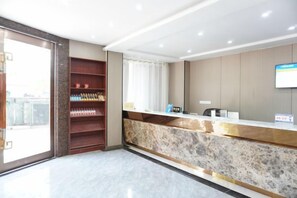 A hotel reception area with a marble counter, a bookshelf with various items, and a large window providing a view of the outside. - Anqing No.1 Pier Hotel (Anqing)