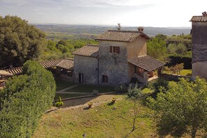 A stone building with a tiled roof, surrounded by greenery and a view of distant hills. - Il Fortino in Monteriggioni (Monteriggioni)