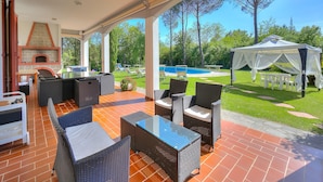 An outdoor patio with wicker furniture, a brick fireplace, and a pool in the background. - Villa Cerbaie in Fucecchio (Fucecchio)