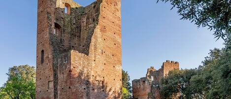 A historic brick tower with arched openings, surrounded by a well-maintained garden and other ruins.