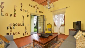 A living room with a sofa, a wooden coffee table, and a television. There is a yellow armchair and a patterned rug. The walls have words written on them.