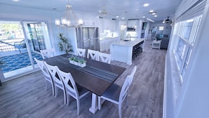 A modern kitchen with white cabinetry, a central island with bar stools, and a dining area with a dark table and white chairs. - Walk to Siesta Key Beach! (Siesta Key)