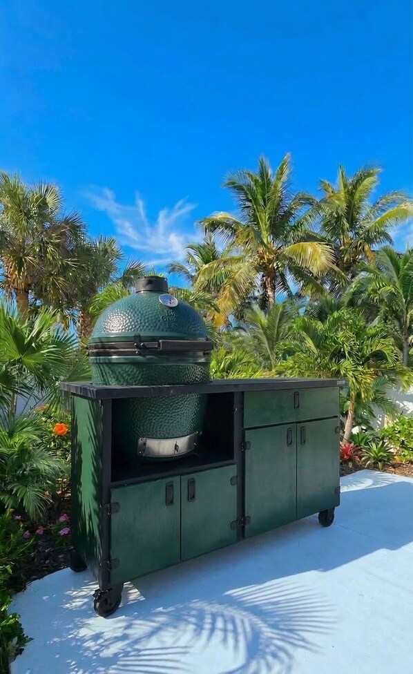 A green outdoor grill with a dome lid, set on a cart, surrounded by palm trees and a clear blue sky. - Walk to Siesta Key Beach! (Siesta Key)