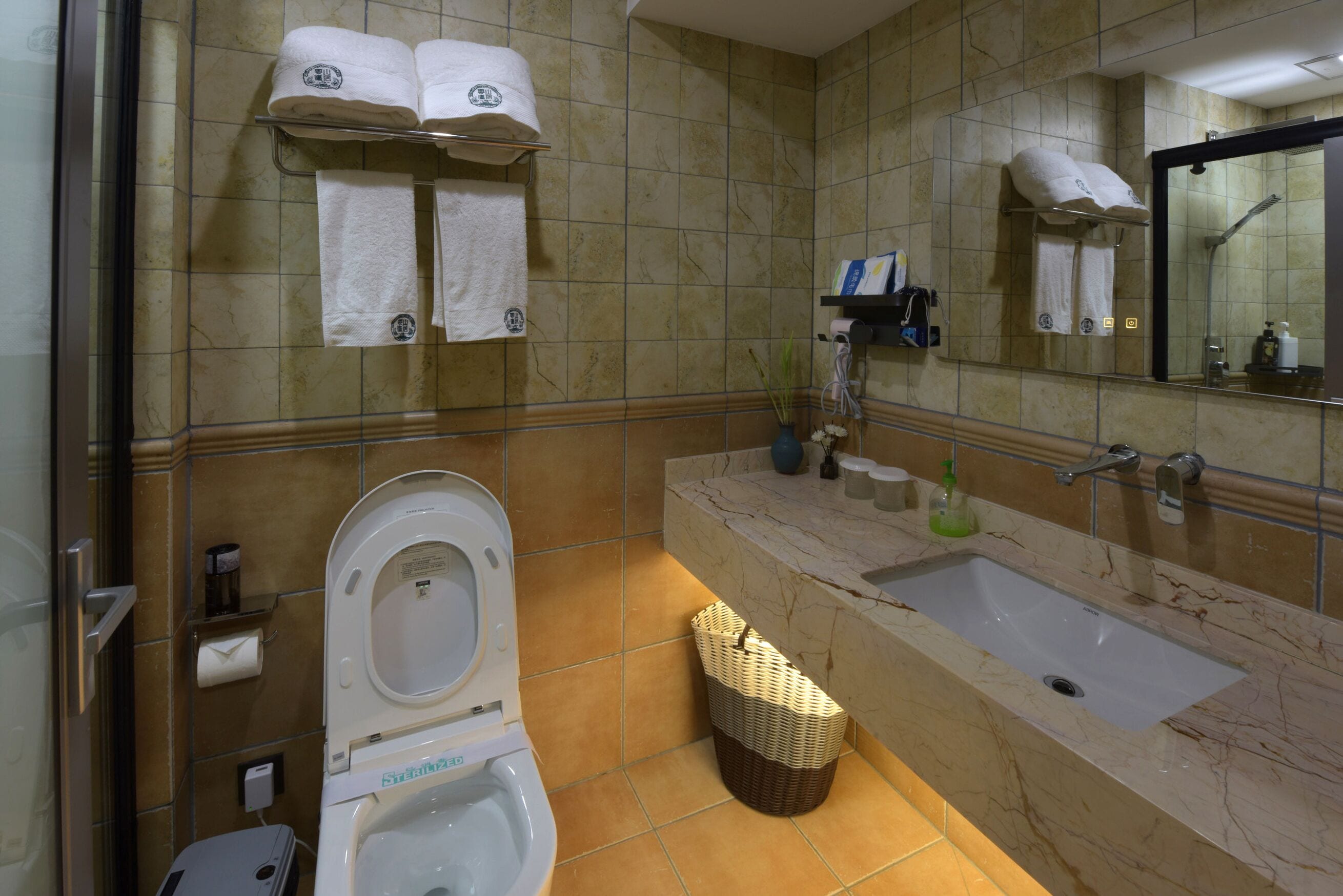 A bathroom with a toilet, sink, and mirror. There are towels hanging on a rack and a basket on the floor.