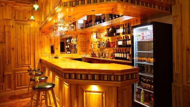 A bar area with wooden walls, a bar counter, stools, and shelves stocked with bottles. - yunlushanju (Xiangxi)