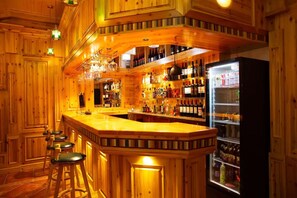 A bar area with wooden walls, a bar counter, stools, and shelves stocked with bottles.