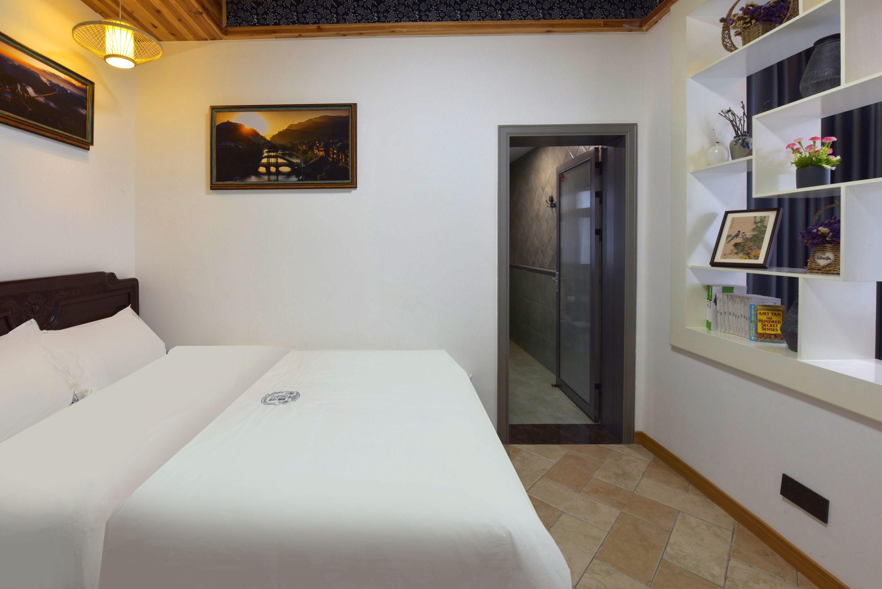 Una cama bien hecha con ropa de cama blanca, un cuadro en la pared y un estante con objetos decorativos.