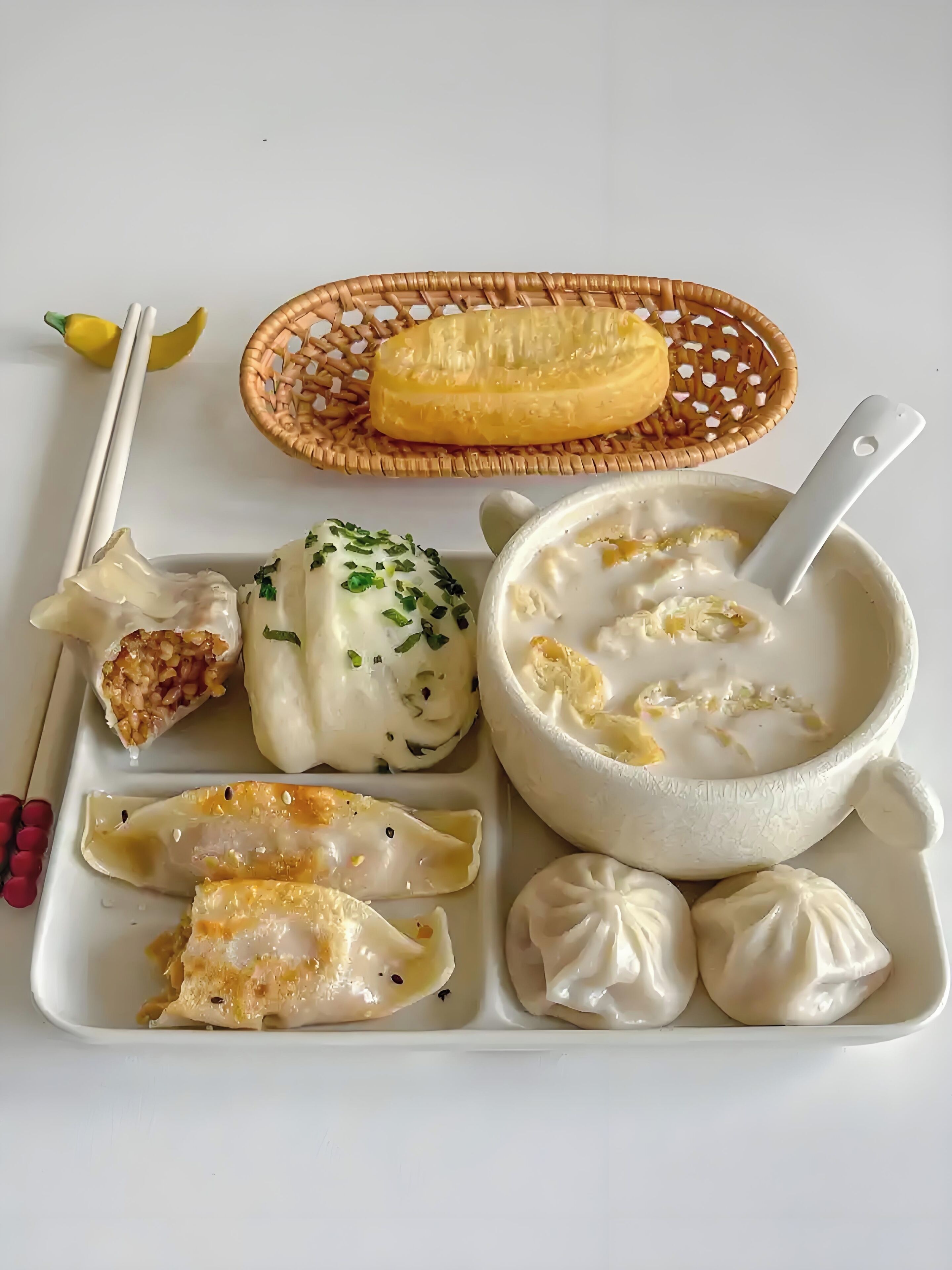 Un vassoio con ravioli, una ciotola di zuppa e un cesto con qualcosa di giallo.