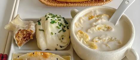 Un vassoio con ravioli, una ciotola di zuppa e un cesto con qualcosa di giallo.