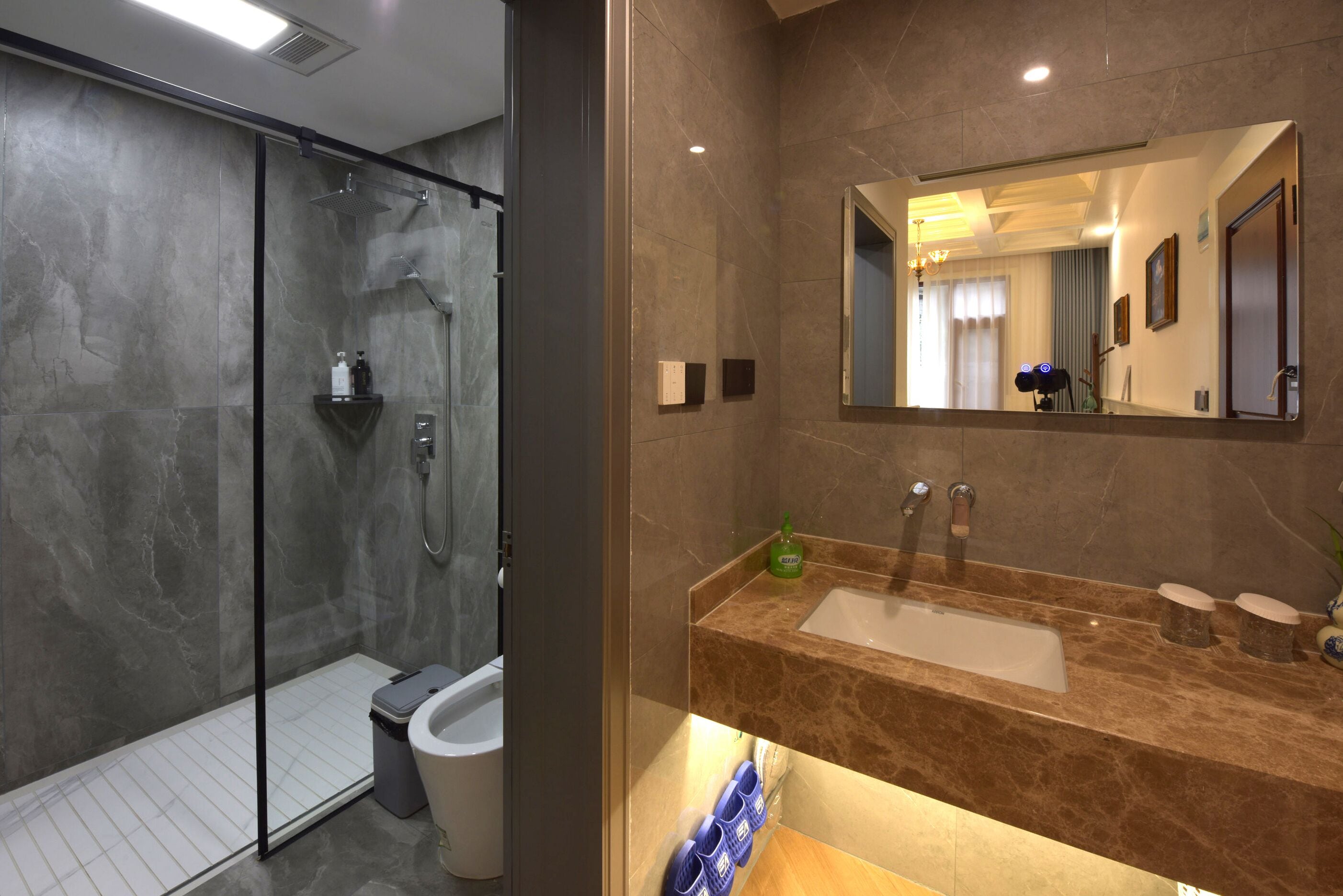 Ein modernes Badezimmer mit einer gläsernen Dusche, einer marmorverkleideten Wand, einem großen Spiegel und einem Waschbecken mit Marmorplatte.