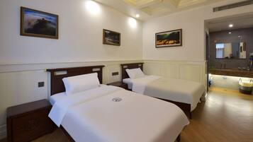 A hotel room with two single beds, a wooden nightstand, a bathroom with a sink and mirror, and framed pictures on the walls.