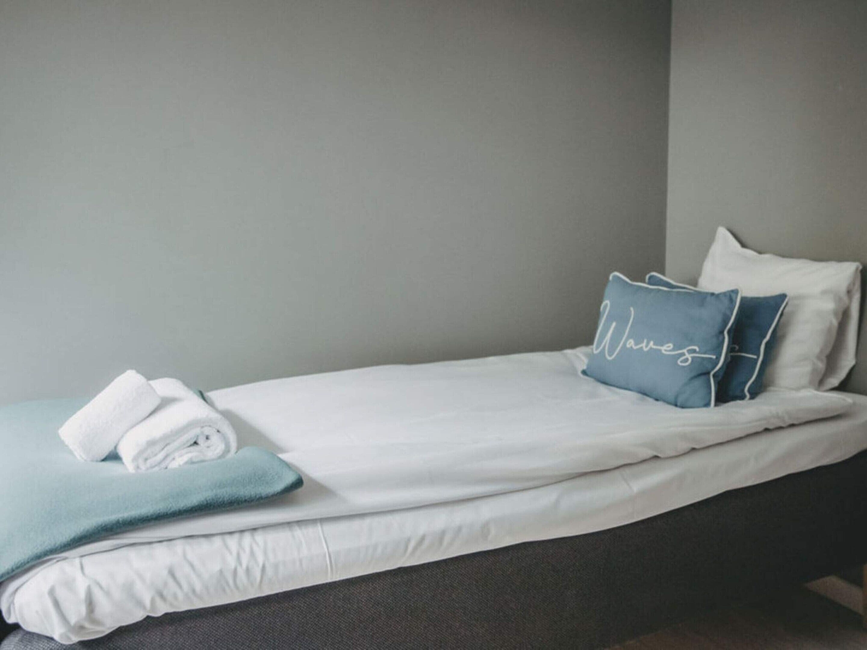 A neatly made bed with white bedding and a blue pillow with the word 'Waves' on it.