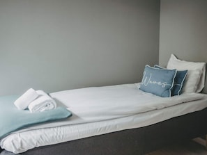 A neatly made bed with white bedding and a blue pillow with the word 'Waves' on it.