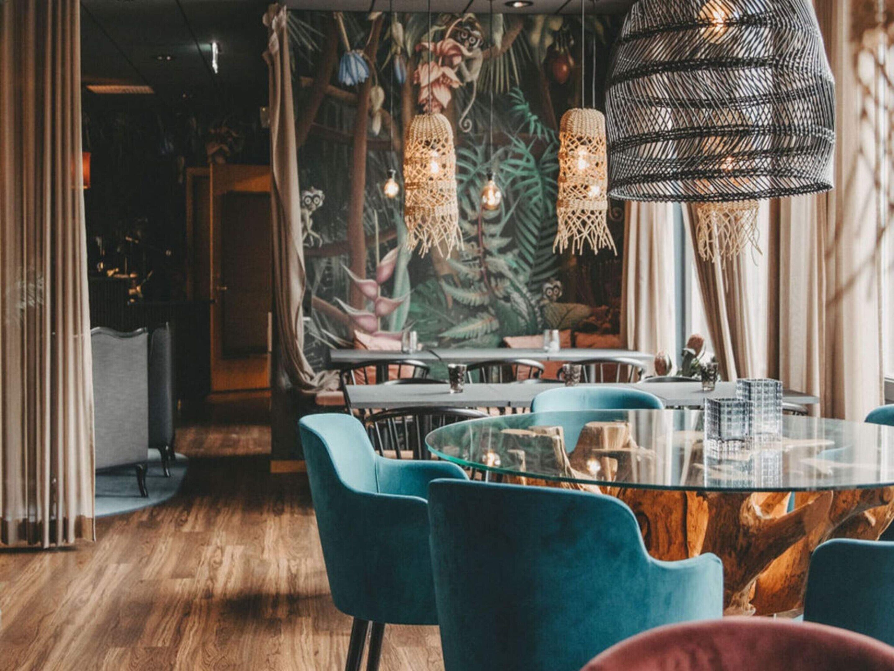 A restaurant interior with round tables, blue chairs, and hanging light fixtures.