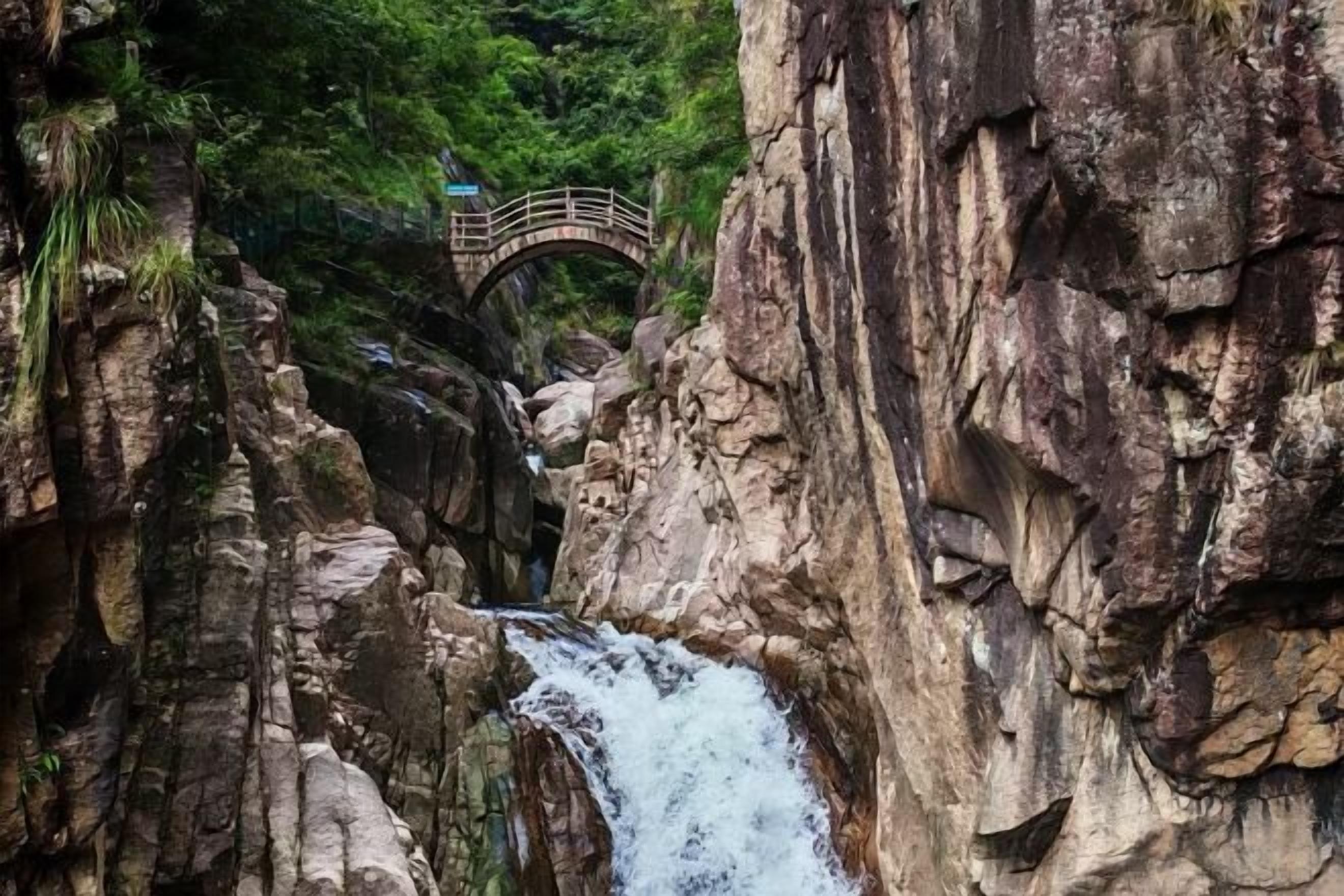 A rocky gorge with a waterfall and a wooden bridge.