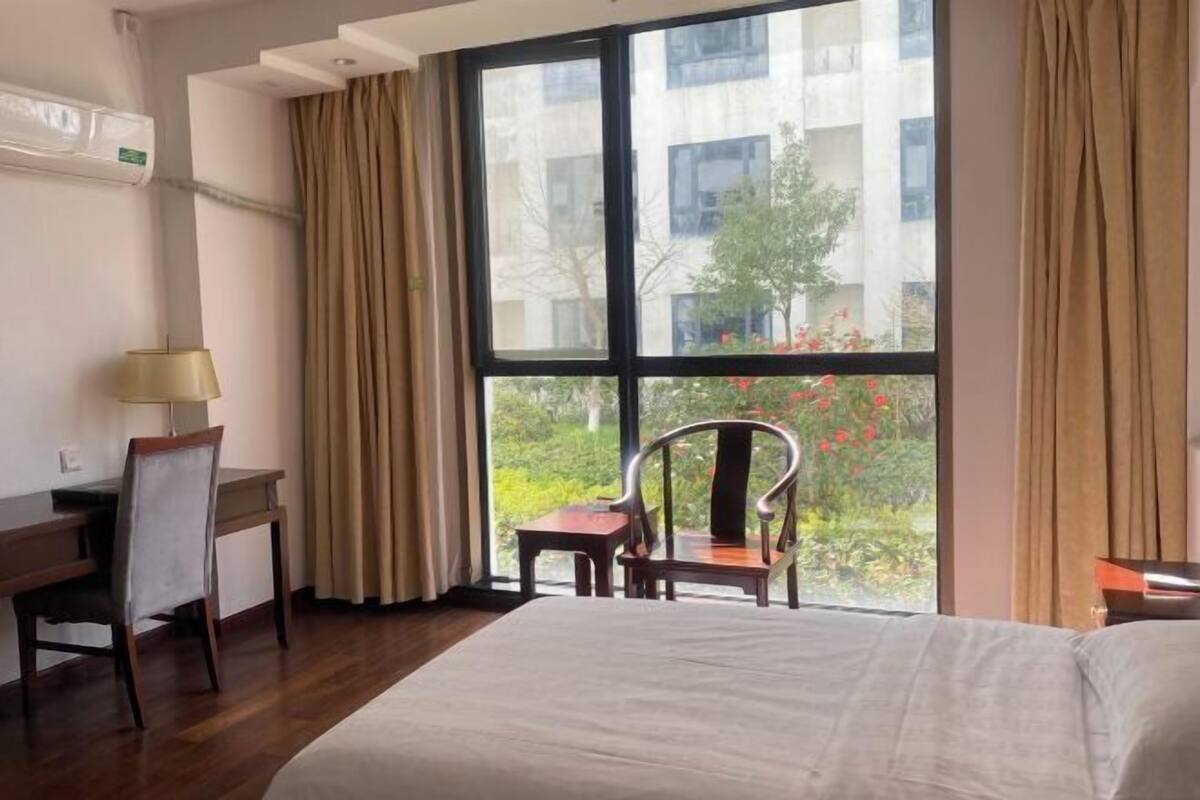 Habitació d'hotel amb una finestra gran, un llit, escriptori, cadira i una taula petita.
