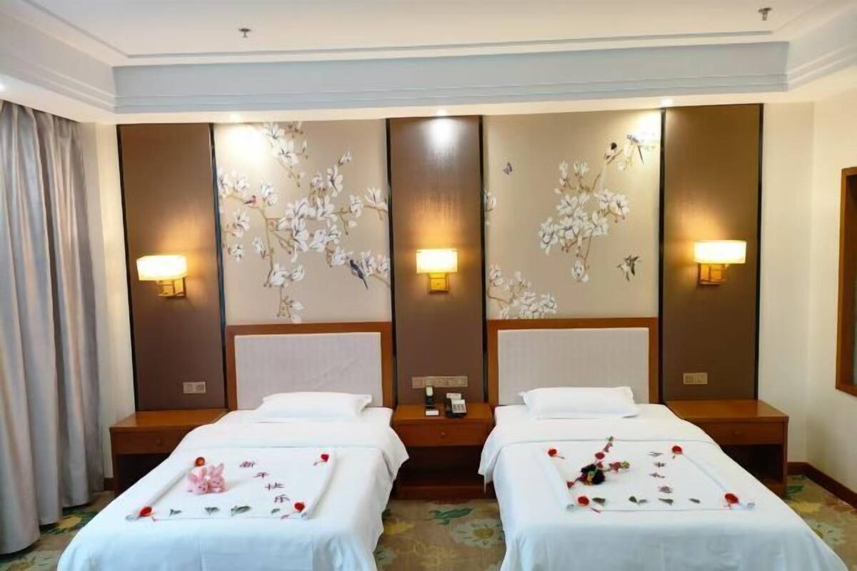 Habitació d'hotel amb dos llits, un mirall gran, làmpades subjectes a la paret i un disseny floral a la paret.