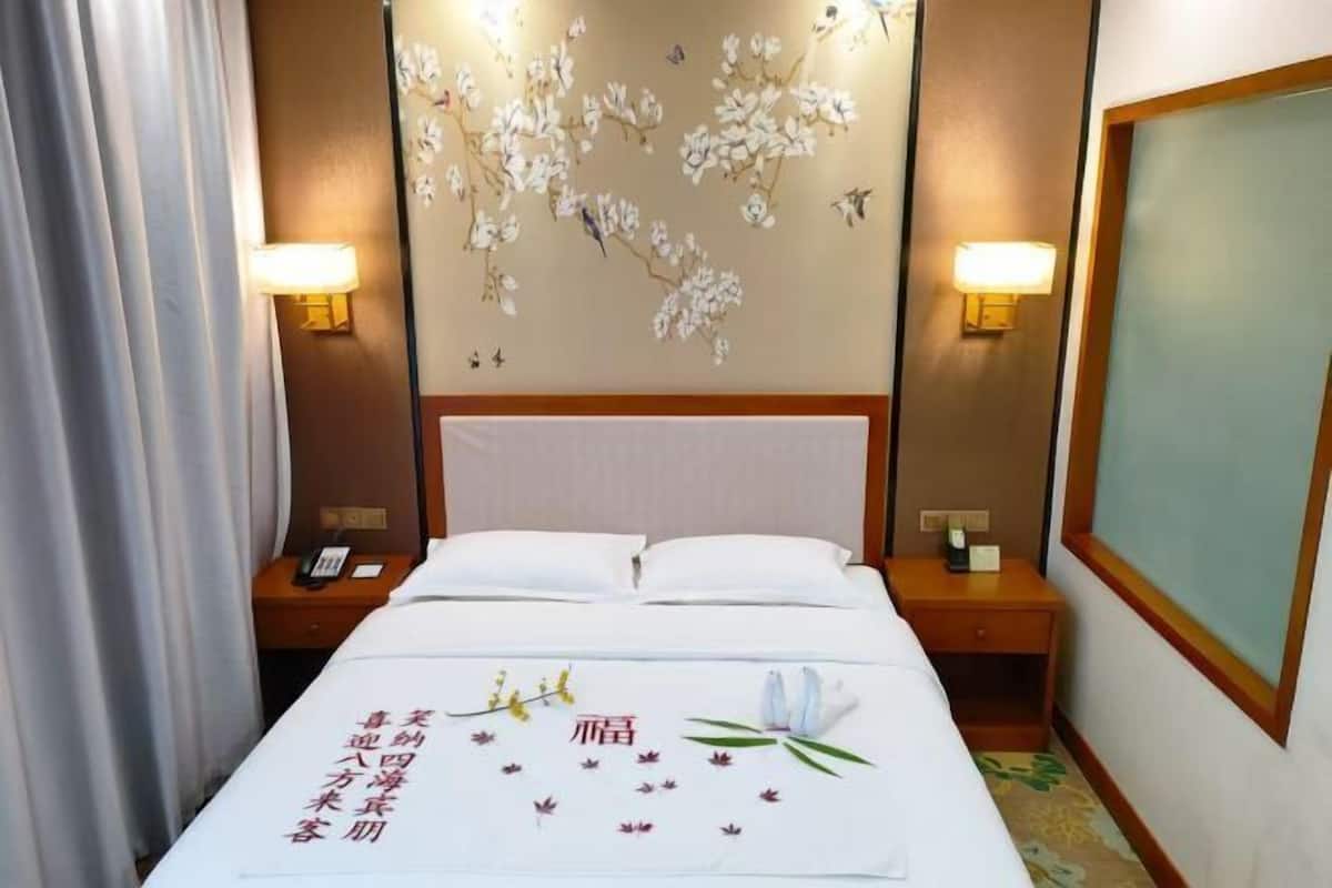Habitació d'hotel amb un llit, dues taules de nit, una làmpada penjada a la paret i una paret decorativa amb motius florals.
