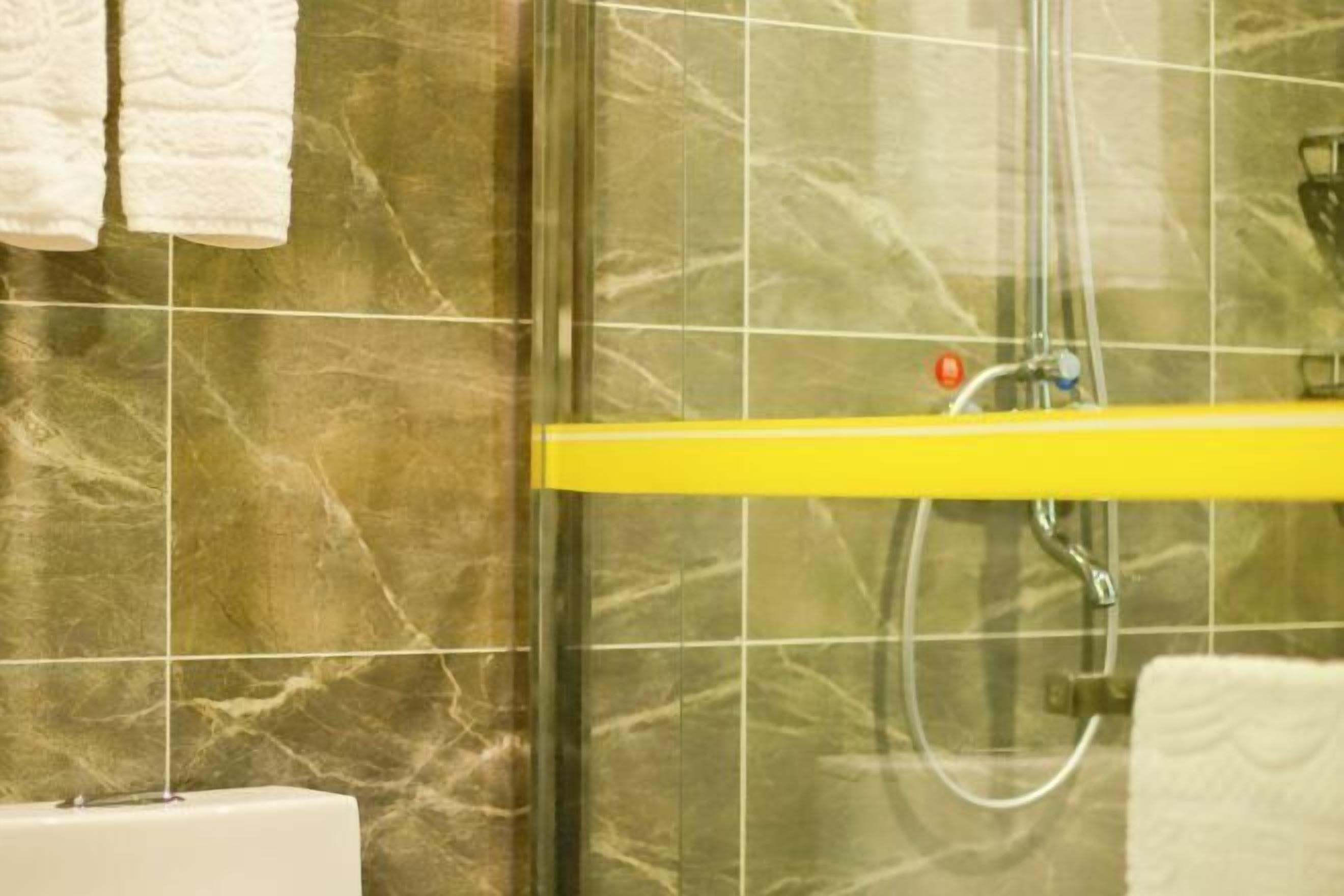 A bathroom with a glass shower enclosure, a yellow shelf, and white towels.