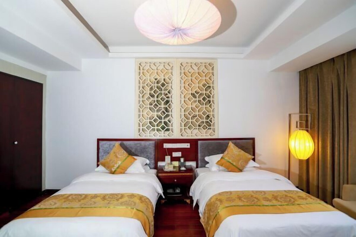 Habitación de hotel con dos camas, una mesita de noche, un panel decorativo en la pared, una lámpara del techo y una lámpara de pared.