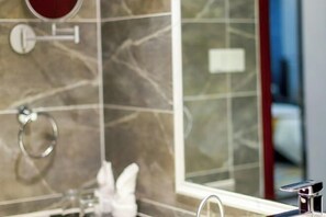Een badkamer met een marmeren wand, een spiegel, een handdoekhouder en een wastafel.