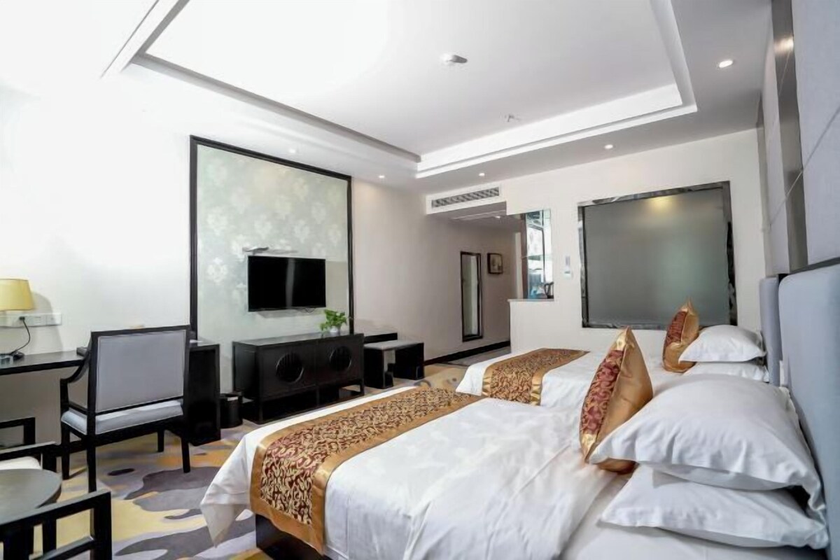 Habitación de hotel con dos camas, un escritorio, una silla, un televisor y un ventanal grande.