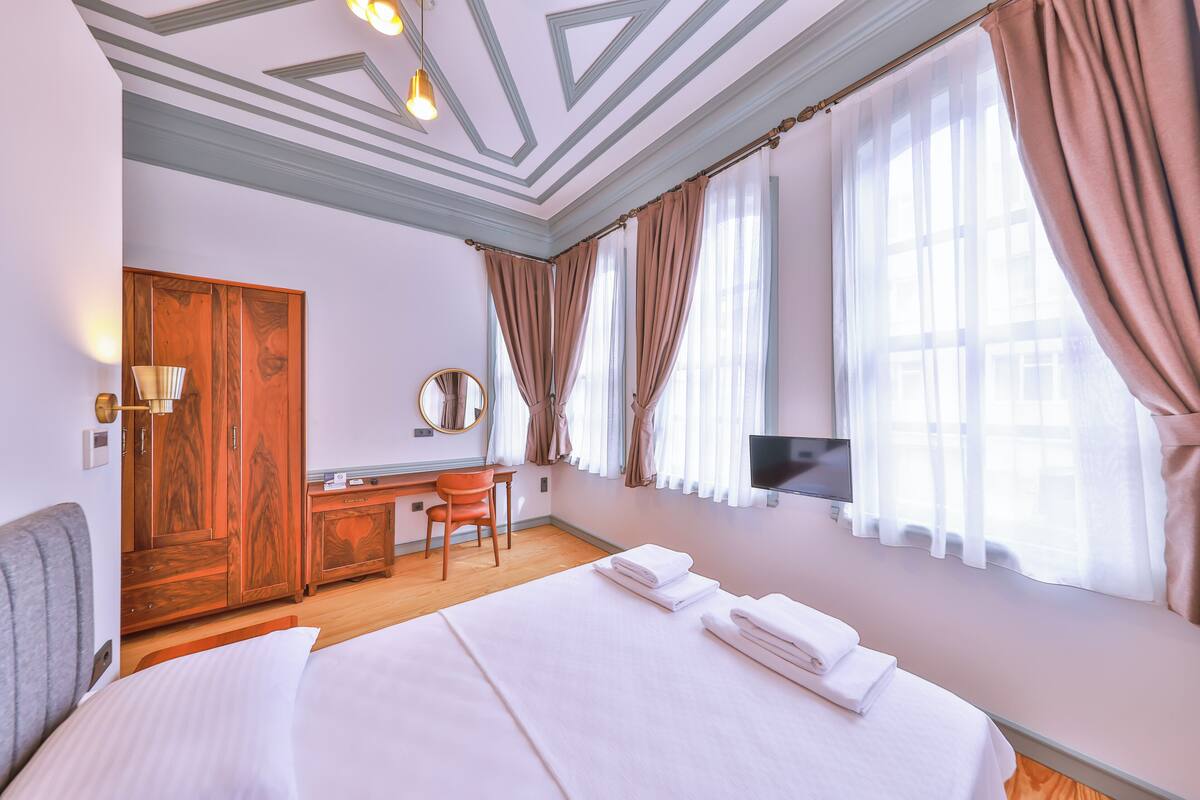 A hotel room with a bed, a desk, a chair, a TV, and a wardrobe.