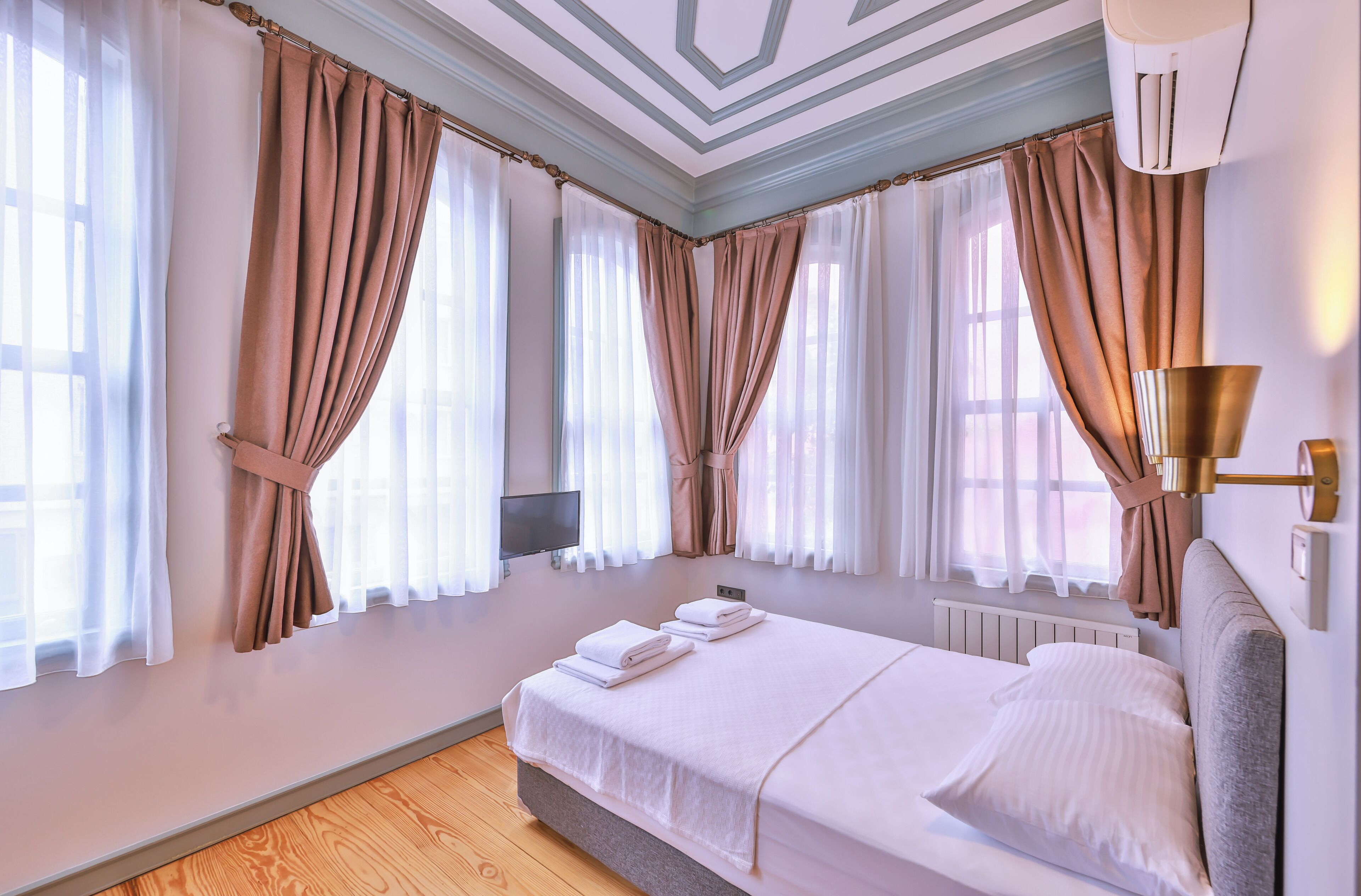 A neatly made bed with white linens, a grey headboard, and a bedside table with a lamp.
