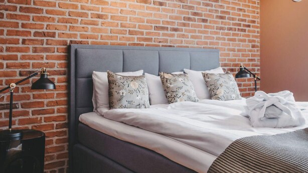 Un lit bien fait, avec une tête de lit grise, une literie blanche et des coussins à motifs floraux.