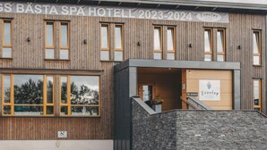 Un hôtel-spa doté d’une façade en bois, d’une entrée en pierre et d’une enseigne indiquant le nom de l’établissement ainsi que les années 2023-2024.
