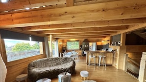 A cozy cabin interior with a large sofa, ottomans, a dining area, and a kitchen. - Chalet, ski lifts base, sauna, terrace, balcony, fireplace or stove, tv, 160m², Villard de Lans (Corrençon-en-Vercors)