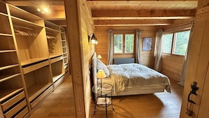 A wooden cabin bedroom with a bed, a small table with a lamp, and a walk-in closet. - Chalet, ski lifts base, sauna, terrace, balcony, fireplace or stove, tv, 160m², Villard de Lans (Corrençon-en-Vercors)