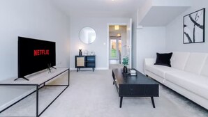Un salon moderne avec un téléviseur à écran plat, un miroir rond, un canapé blanc et une table basse.