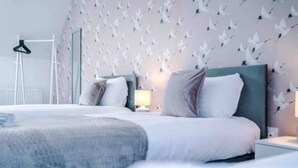 Une chambre d’hôtel moderne avec deux lits, une armoire et un mur décoré d’un motif représentant des oiseaux.