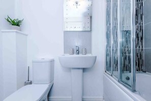 A modern bathroom with a white sink, toilet, and shower. - Lovely three bed home Manchester (Bury)