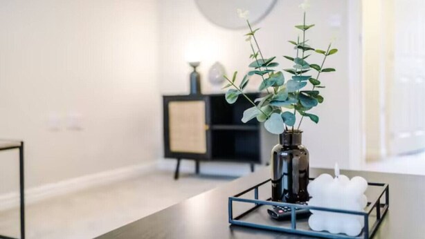 Un intérieur moderne avec une table en bois foncé, un vase contenant des plantes vertes et une bougie blanche posée sur un plateau.