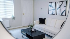 Un salon moderne avec un canapé blanc, une table basse noire et des œuvres d’art abstraites accrochées au mur.