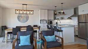A modern kitchen with white cabinets, a stainless steel refrigerator, and a central island with bar stools. - Le Zéphyr - Waterfront (Beaulac-Garthby)