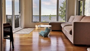 A spacious living room with a large sliding glass door leading to a balcony, a round coffee table, and a beige sofa. - Le Zéphyr - Waterfront (Beaulac-Garthby)