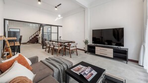 Ett rymligt vardagsrum med ett matbord, stolar, en soffa, ett soffbord, en TV och en trappa som leder till ett annat rum.