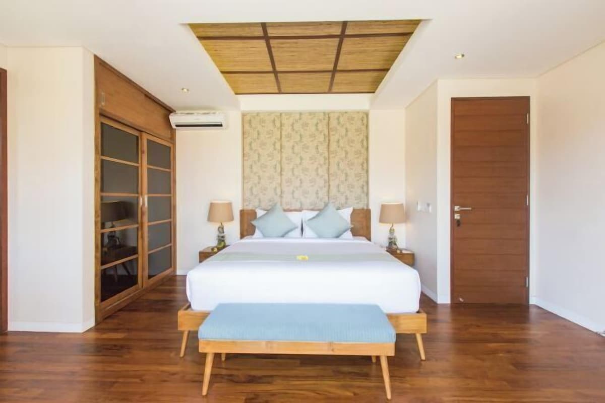 A bedroom with a large bed, wooden floor, a ceiling with a grid pattern, a wardrobe with glass doors, and a door with a wooden panel.