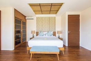 A bedroom with a large bed, wooden floor, a ceiling with a grid pattern, a wardrobe with glass doors, and a door with a wooden panel. - Beautiful Bali Villas (Bali)