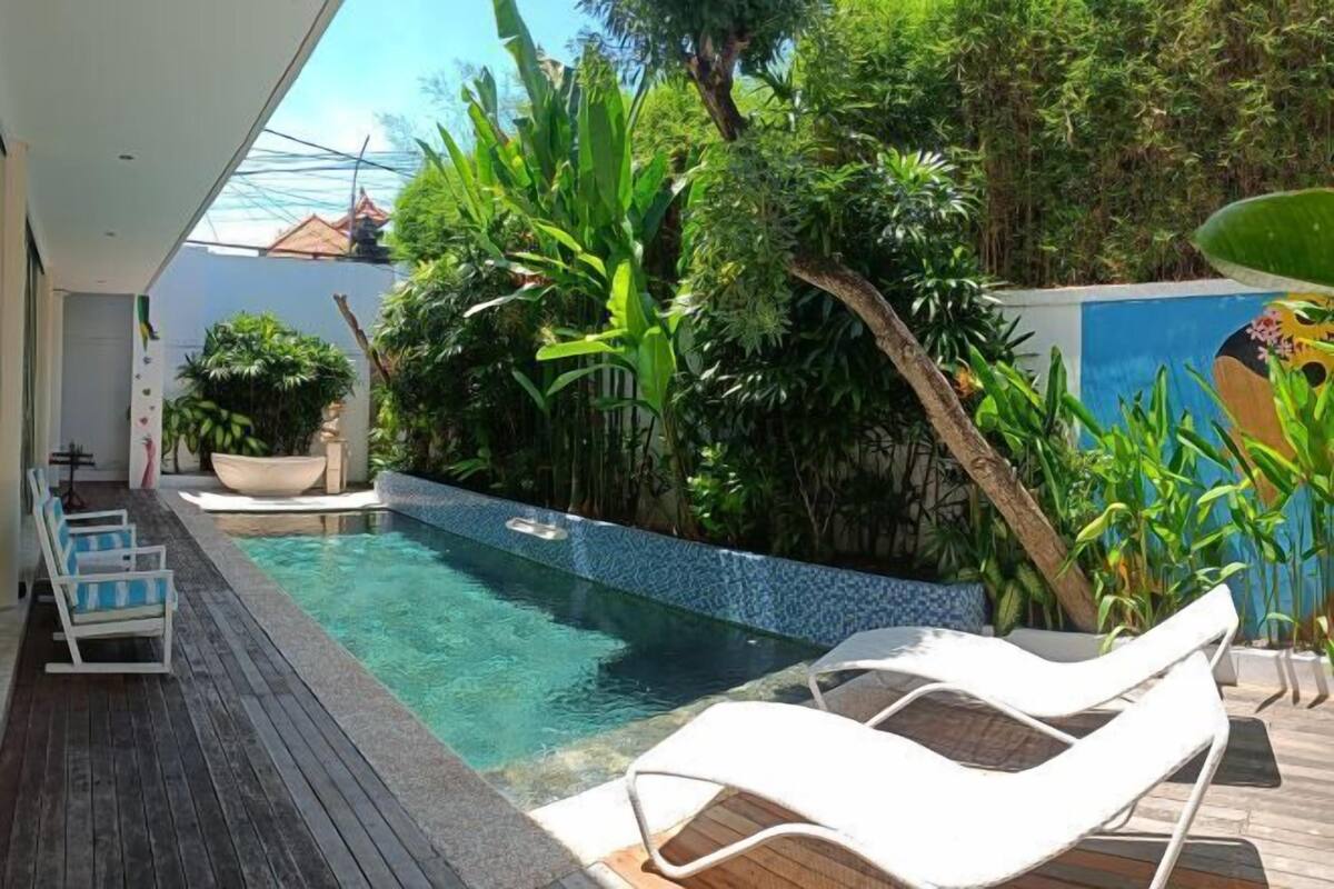 A pool with lounge chairs, surrounded by lush greenery and a tiled deck.